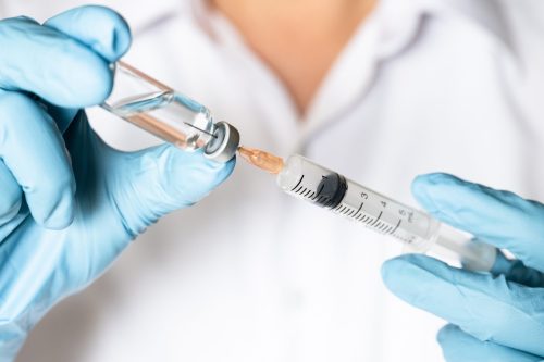 Nurse or doctor hand in blue glove holding flu, measles vaccine